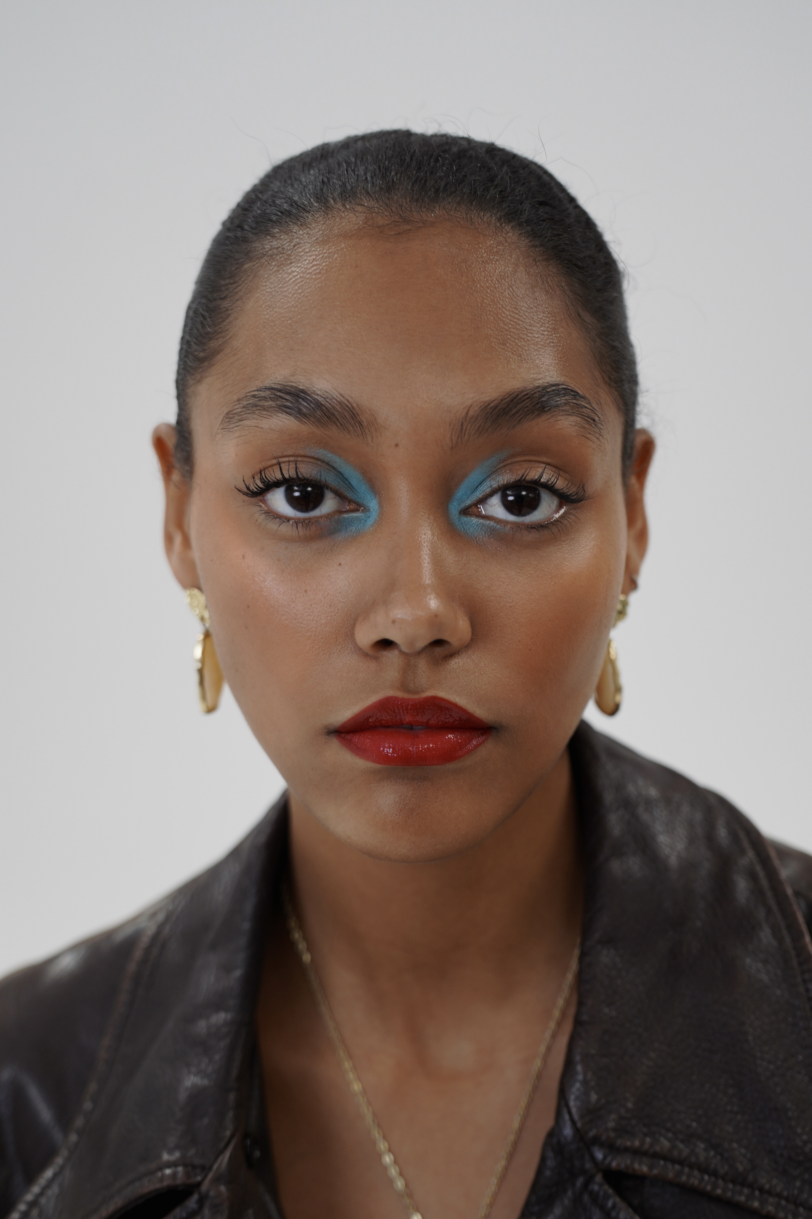 Beauty portrait with turquoise eyeshadow, red lips, and gold hoop earrings in black leather jacket
