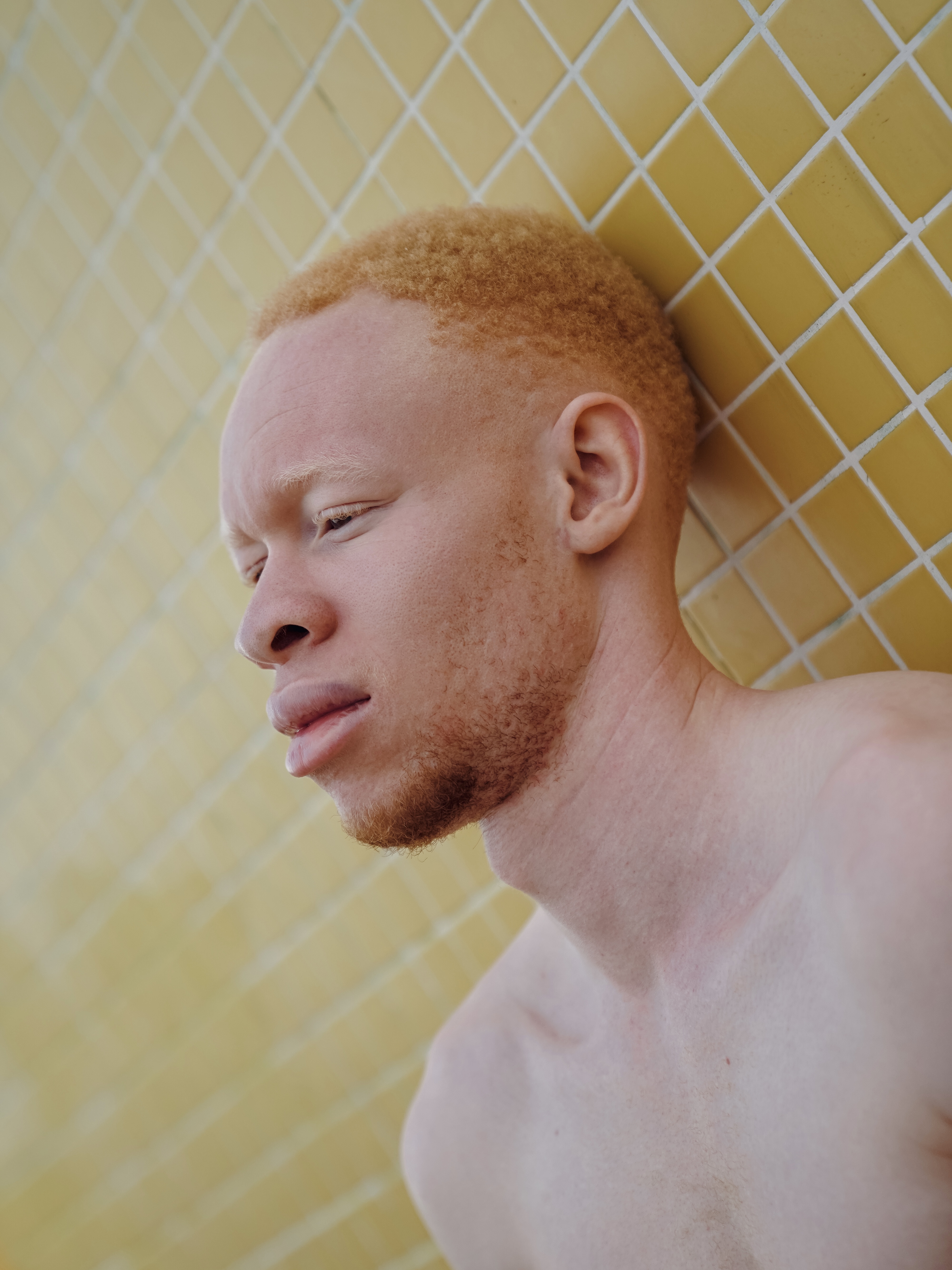 Side profile portrait against yellow tile background with diamond pattern