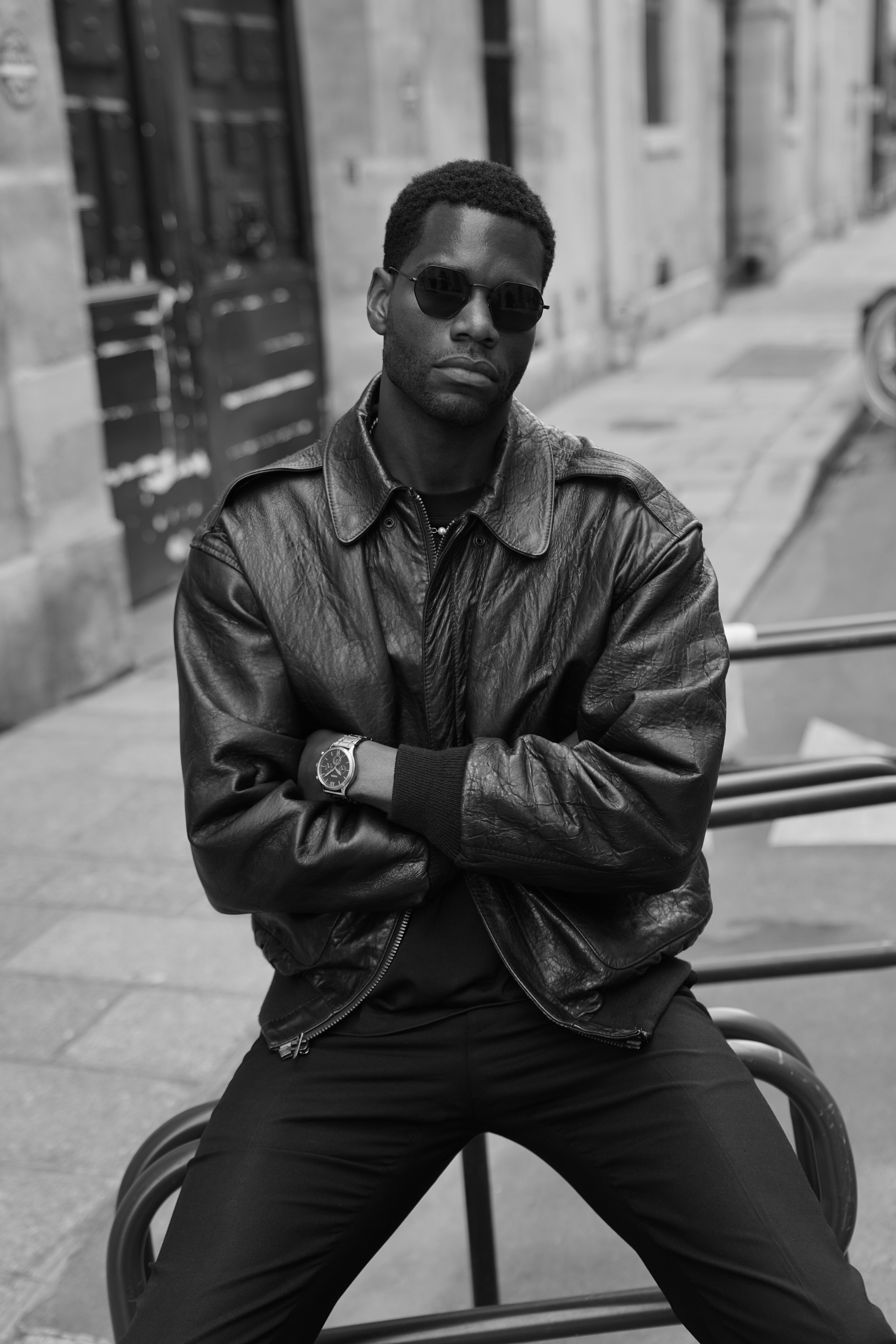 Man in leather jacket and sunglasses sitting on chair with arms crossed