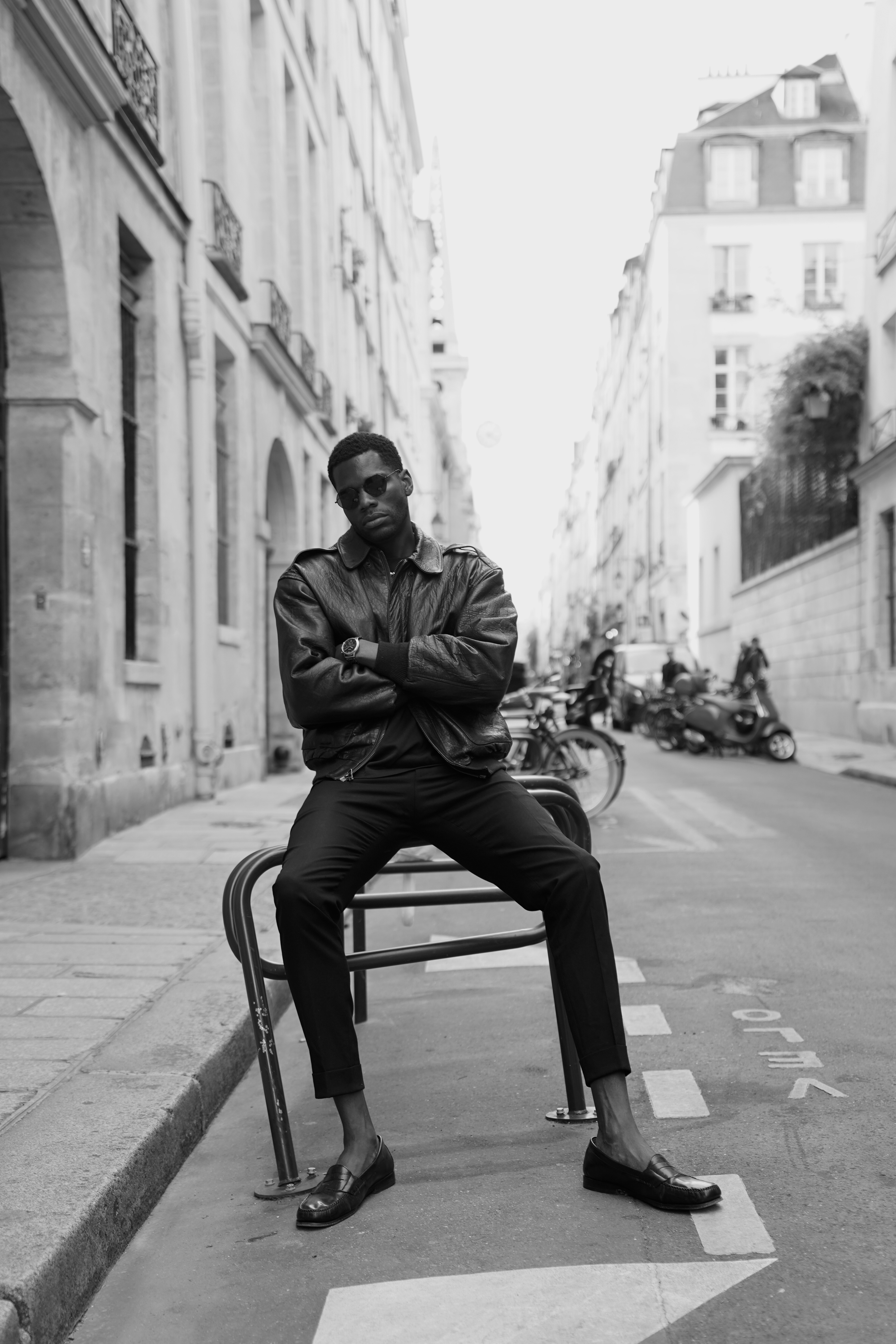 Man in leather jacket and sunglasses sitting on chair in Parisian street